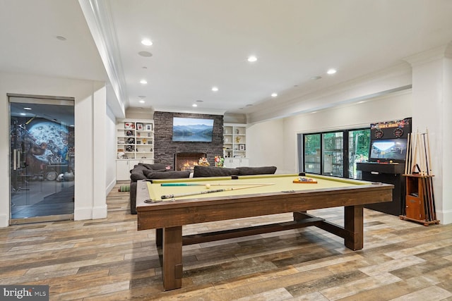 rec room featuring a stone fireplace, crown molding, built in features, light wood-type flooring, and pool table