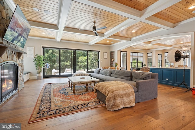 living room featuring beam ceiling, ceiling fan, a fireplace, and light wood-type flooring