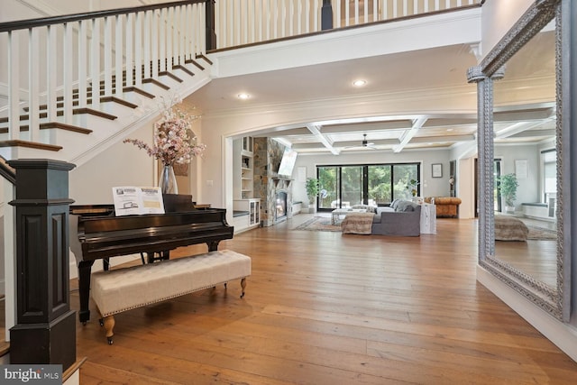 miscellaneous room with coffered ceiling, ceiling fan, beam ceiling, hardwood / wood-style floors, and a stone fireplace