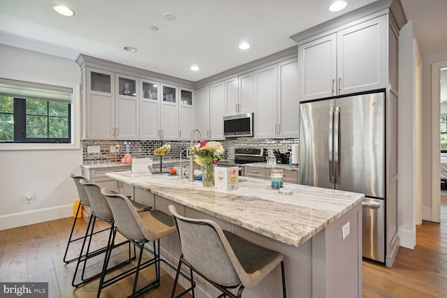 kitchen with light stone countertops, a kitchen bar, light wood-type flooring, stainless steel appliances, and an island with sink