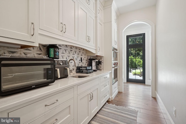 kitchen featuring sink, light hardwood / wood-style flooring, decorative backsplash, white cabinetry, and stainless steel double oven