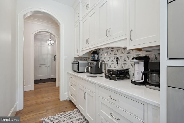 kitchen featuring white cabinets, light hardwood / wood-style floors, ornamental molding, and tasteful backsplash