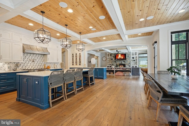 kitchen featuring ventilation hood, decorative light fixtures, a kitchen island with sink, white cabinets, and wood ceiling