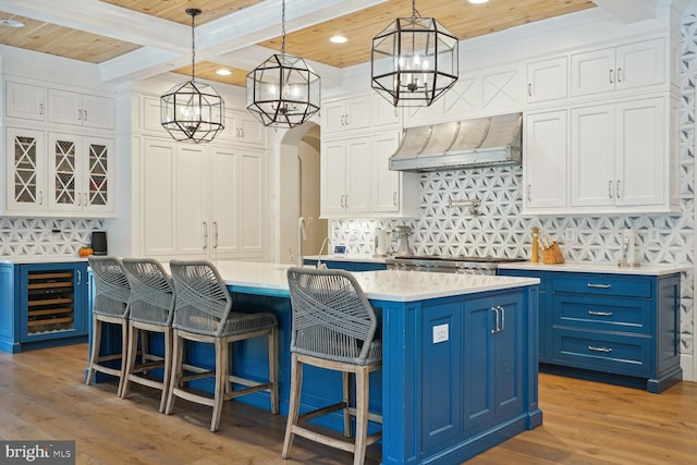 kitchen with beverage cooler, beamed ceiling, blue cabinets, wood ceiling, and custom range hood