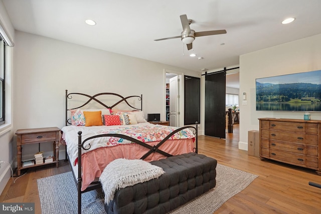 bedroom featuring ceiling fan, a barn door, a spacious closet, light hardwood / wood-style floors, and a closet