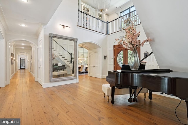 misc room with crown molding, a towering ceiling, light hardwood / wood-style floors, and an inviting chandelier