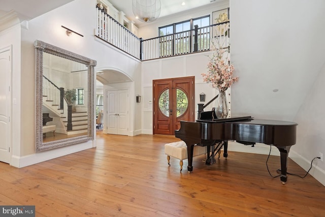 foyer entrance with light hardwood / wood-style floors, ornate columns, crown molding, and a high ceiling