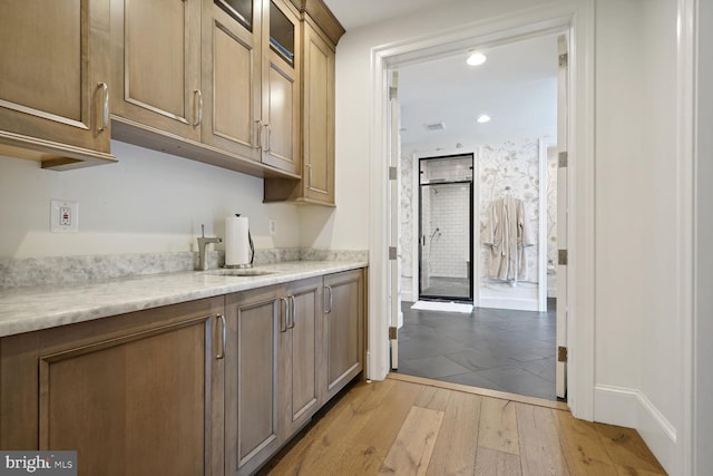 kitchen with light stone counters, sink, and light hardwood / wood-style flooring