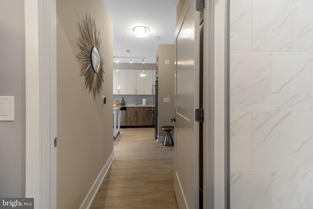 hall with light wood-type flooring, baseboards, and track lighting