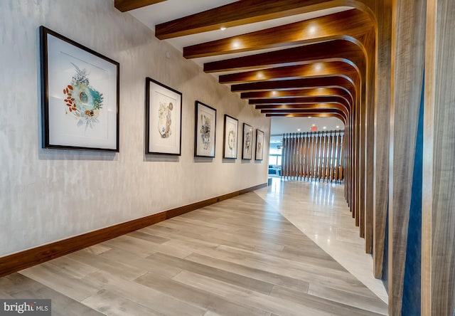 hall featuring beam ceiling, light wood finished floors, and baseboards