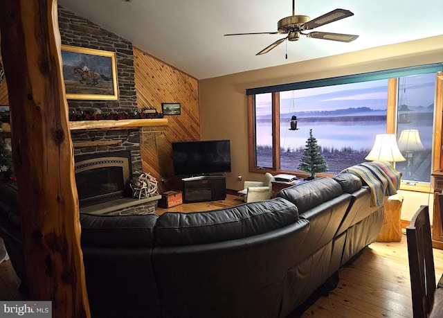 living room featuring a stone fireplace, lofted ceiling, hardwood / wood-style floors, wood walls, and ceiling fan