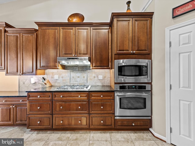 kitchen with appliances with stainless steel finishes, light tile patterned flooring, backsplash, and dark stone countertops