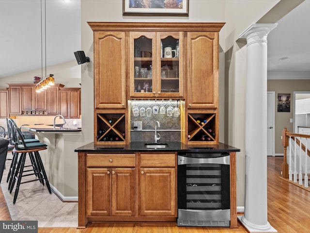 bar featuring light hardwood / wood-style flooring, ornate columns, hanging light fixtures, vaulted ceiling, and beverage cooler