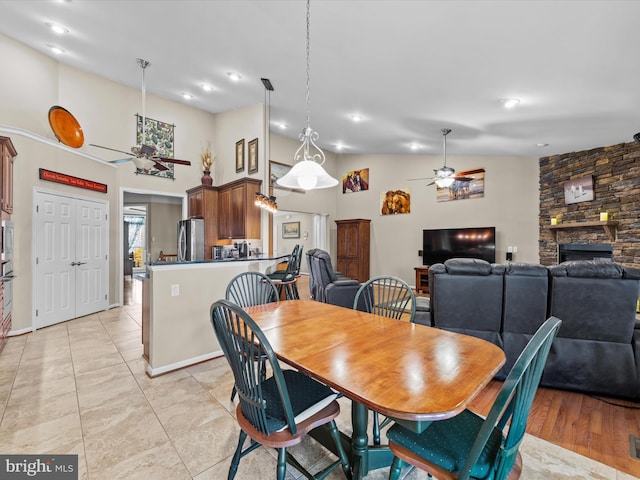 dining area with ceiling fan, light wood-type flooring, a fireplace, and lofted ceiling