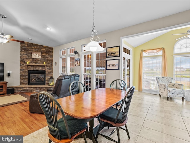 dining room featuring ceiling fan, light wood-type flooring, a stone fireplace, and lofted ceiling