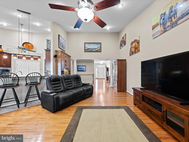 living room featuring ceiling fan, light wood-type flooring, and a towering ceiling