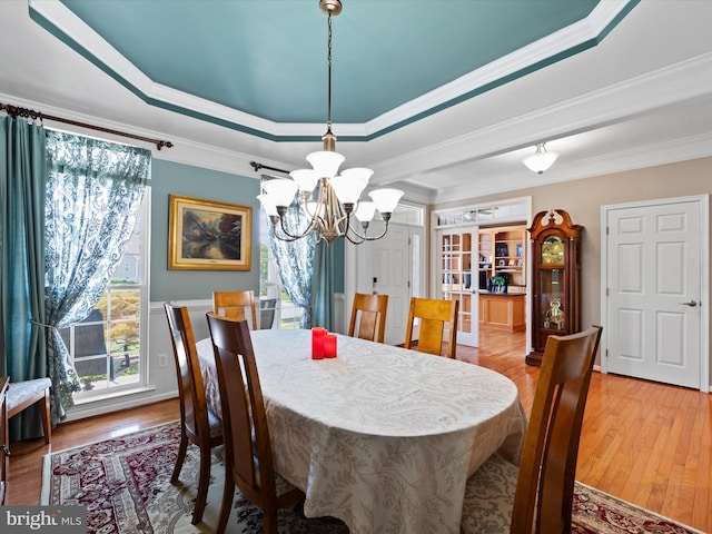 dining space featuring light hardwood / wood-style flooring, crown molding, and a raised ceiling