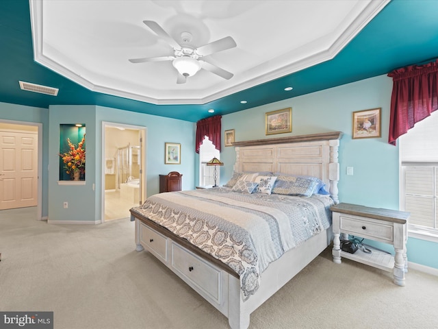 bedroom with light carpet, a tray ceiling, ceiling fan, and ensuite bathroom