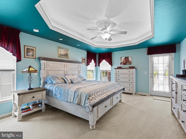 bedroom with ceiling fan, access to exterior, multiple windows, and a tray ceiling