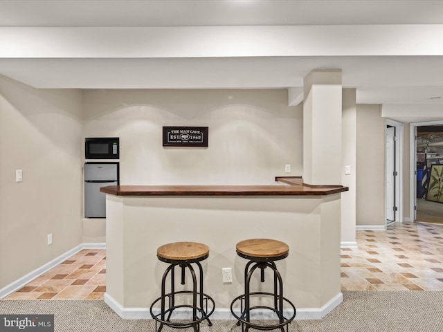 kitchen featuring stainless steel fridge, black microwave, light tile patterned floors, and a breakfast bar area