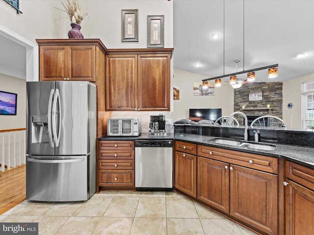 kitchen featuring light wood-type flooring, stainless steel appliances, hanging light fixtures, dark stone counters, and sink