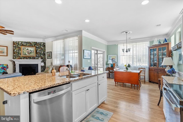 kitchen with a center island with sink, hanging light fixtures, sink, appliances with stainless steel finishes, and white cabinetry