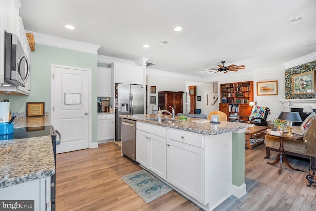 kitchen with appliances with stainless steel finishes, light stone counters, sink, white cabinetry, and an island with sink