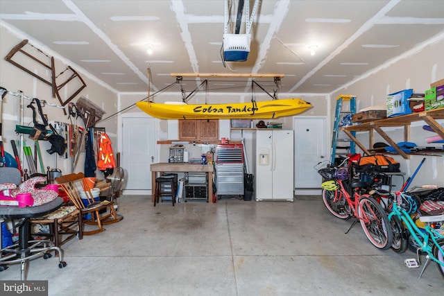 garage featuring a workshop area, white fridge with ice dispenser, and a garage door opener