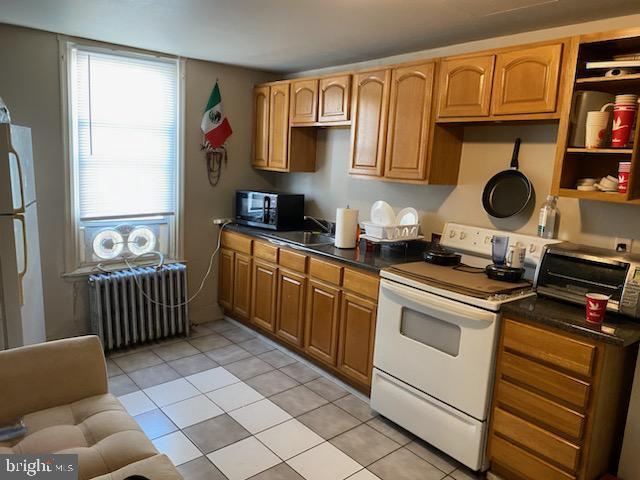 kitchen with radiator heating unit, light tile patterned flooring, white appliances, and sink