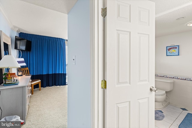 bathroom featuring a textured ceiling, toilet, tile walls, and tile patterned floors