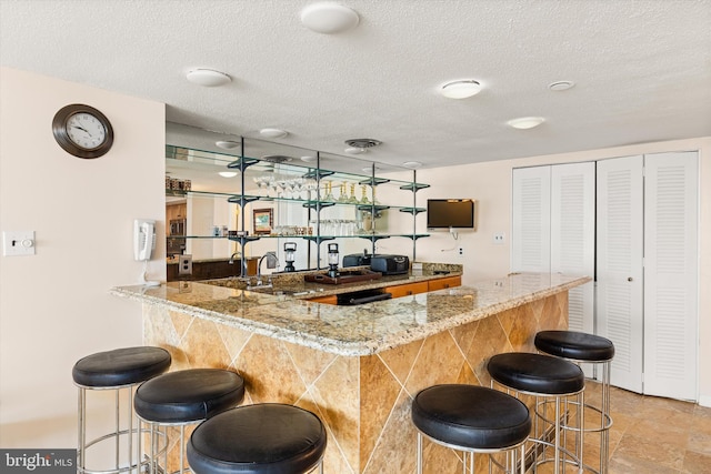 bar featuring a textured ceiling, sink, and stone countertops