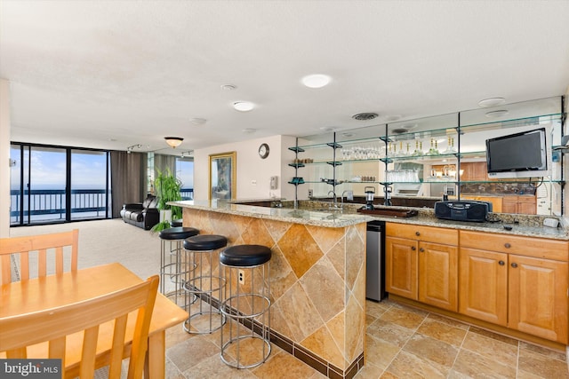 kitchen featuring light stone counters, a wall of windows, a breakfast bar area, and an island with sink