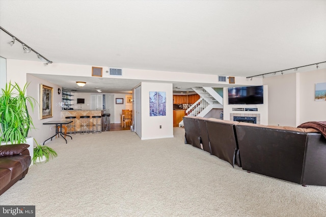 living room with a tiled fireplace, rail lighting, and light colored carpet