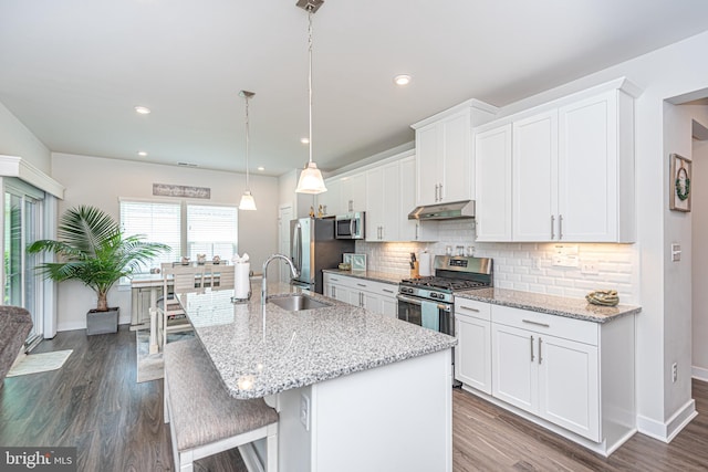 kitchen featuring appliances with stainless steel finishes, a center island with sink, white cabinets, and decorative light fixtures