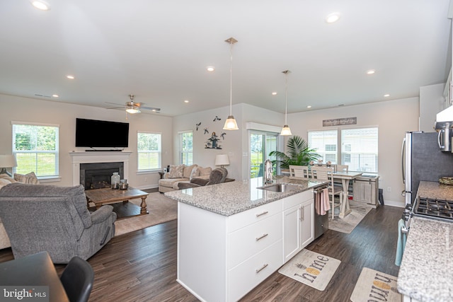 kitchen featuring sink, white cabinetry, decorative light fixtures, an island with sink, and light stone countertops