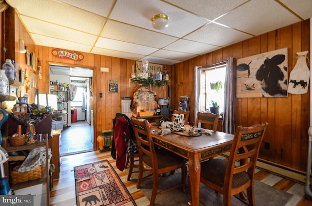 dining area featuring a paneled ceiling, radiator, a baseboard heating unit, light hardwood / wood-style flooring, and wood walls