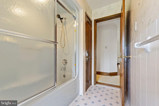 bathroom featuring combined bath / shower with glass door and tile walls