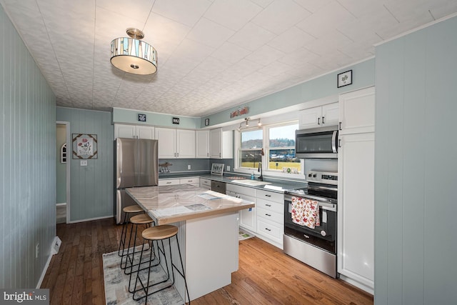 kitchen featuring appliances with stainless steel finishes, a breakfast bar, hardwood / wood-style flooring, white cabinets, and a kitchen island