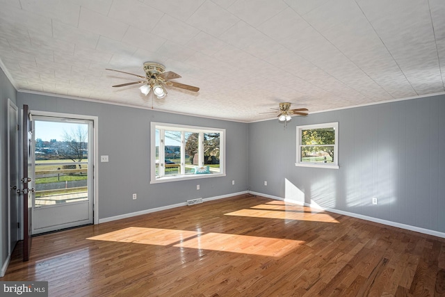 empty room with a wealth of natural light, hardwood / wood-style floors, ceiling fan, and ornamental molding