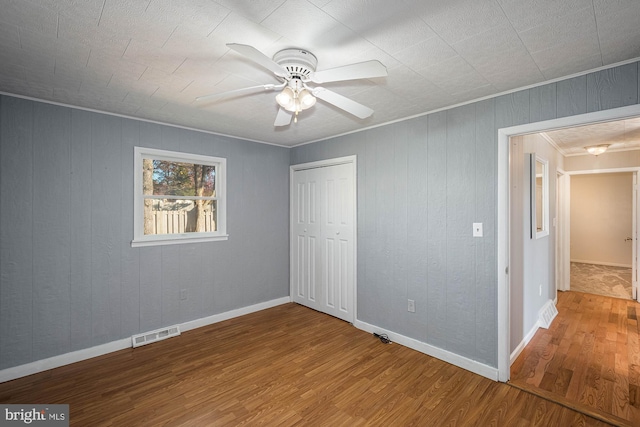 unfurnished bedroom featuring wood-type flooring, a closet, ceiling fan, and crown molding