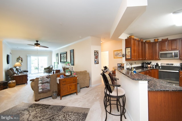 kitchen with kitchen peninsula, appliances with stainless steel finishes, light carpet, dark stone counters, and a breakfast bar area