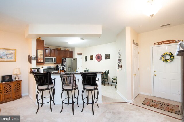 kitchen with a kitchen breakfast bar, light colored carpet, kitchen peninsula, and appliances with stainless steel finishes