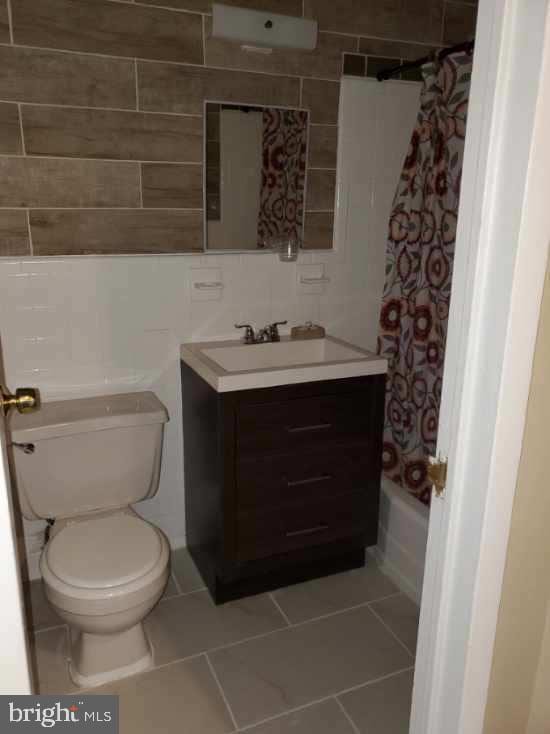 full bathroom with vanity, shower / bath combo with shower curtain, tile walls, tile patterned flooring, and toilet