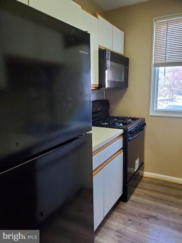 kitchen featuring white cabinets, black appliances, and light wood-type flooring