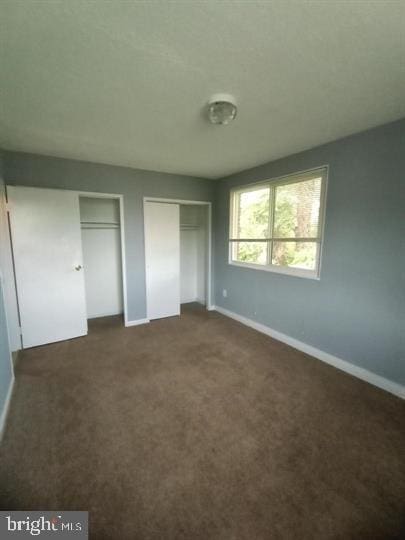 unfurnished bedroom featuring dark carpet and two closets