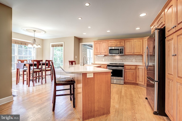 kitchen with tasteful backsplash, stainless steel appliances, sink, a center island with sink, and a chandelier