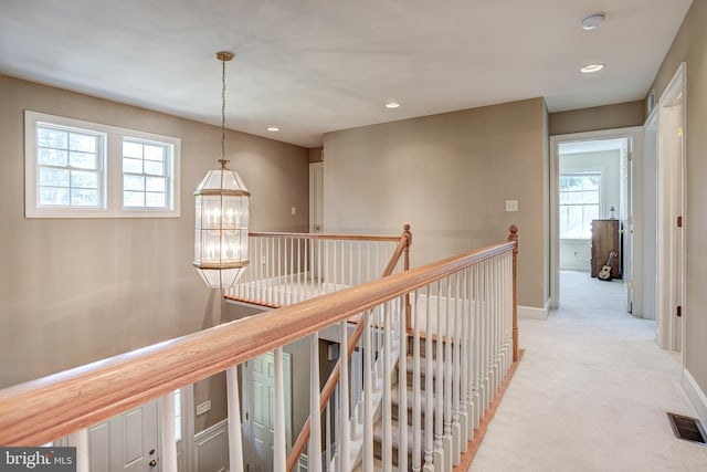 corridor with plenty of natural light, light colored carpet, and a notable chandelier