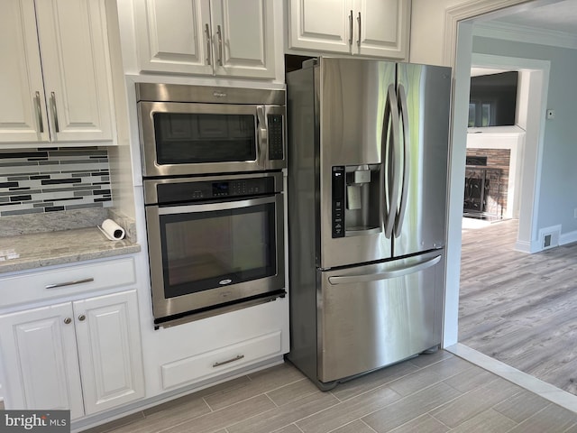 kitchen with white cabinetry, light stone countertops, stainless steel refrigerator with ice dispenser, and ornamental molding