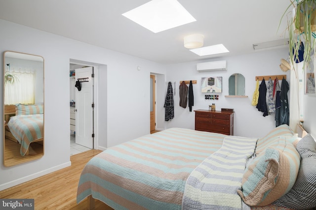 bedroom with a skylight, ensuite bathroom, light hardwood / wood-style flooring, and a wall mounted air conditioner