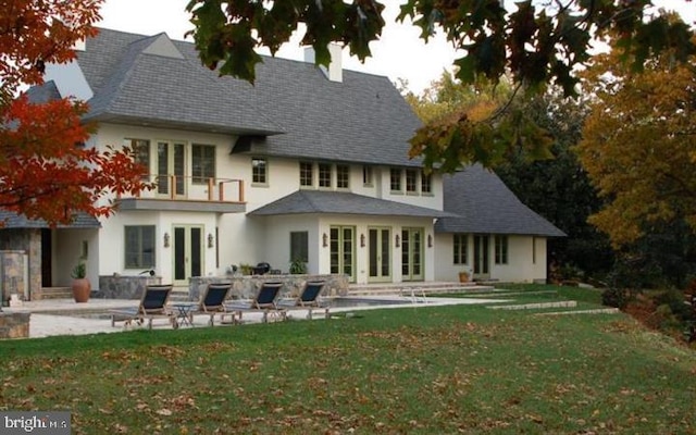 back of property featuring french doors, a patio, a balcony, and a lawn